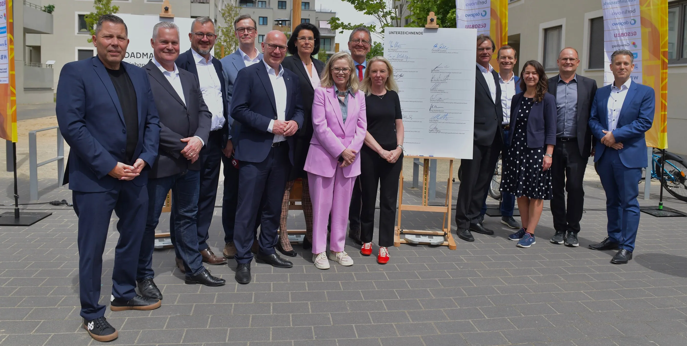 Der Regierende Bürgermeister Kai Wegner posiert bei einem Pressetermin mit weiteren Senatsmitgliedern und den GeschäftsführerInnen der landeseigenen Wohnungsunternehmen in einem Neubauquartier. Zudem ist eine überdimensionale Tafel zu sehen, auf der alle Personen unterschrieben haben. Foto: Tina Merkau