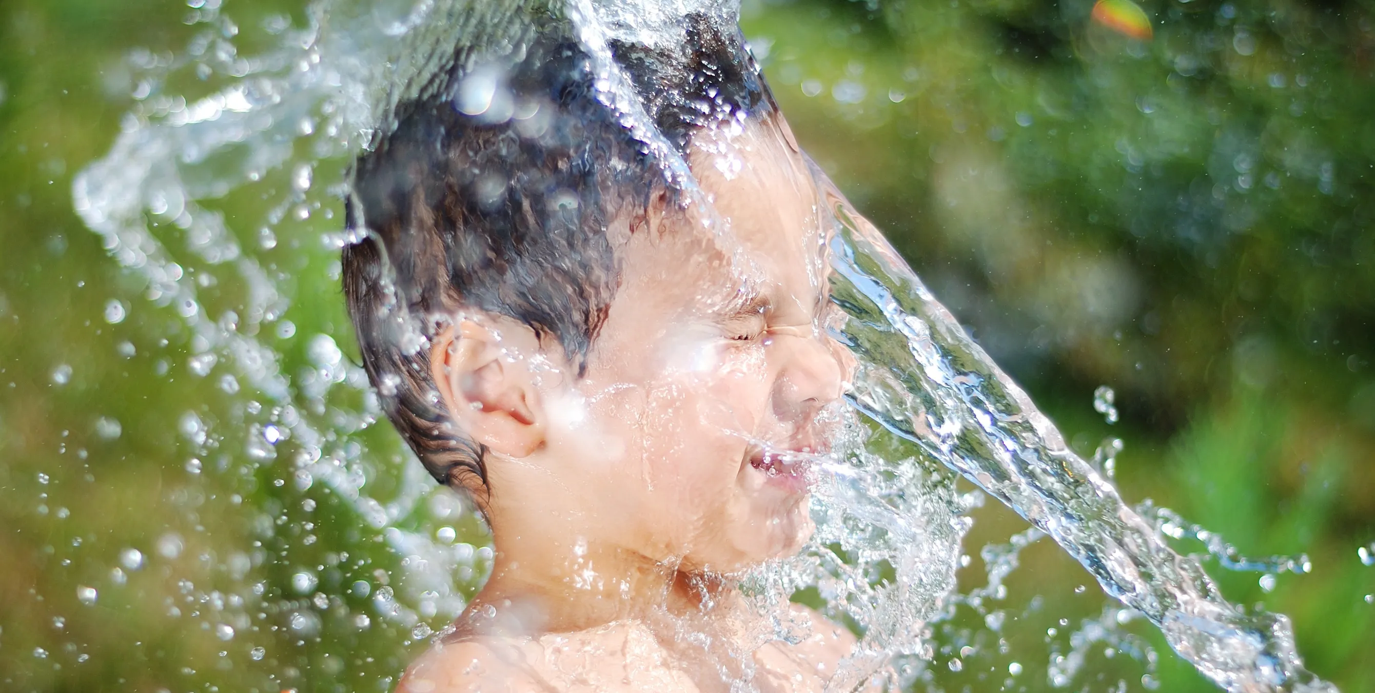 Junge auf Wasserspielplatz bekommt Wasser ins Gesicht