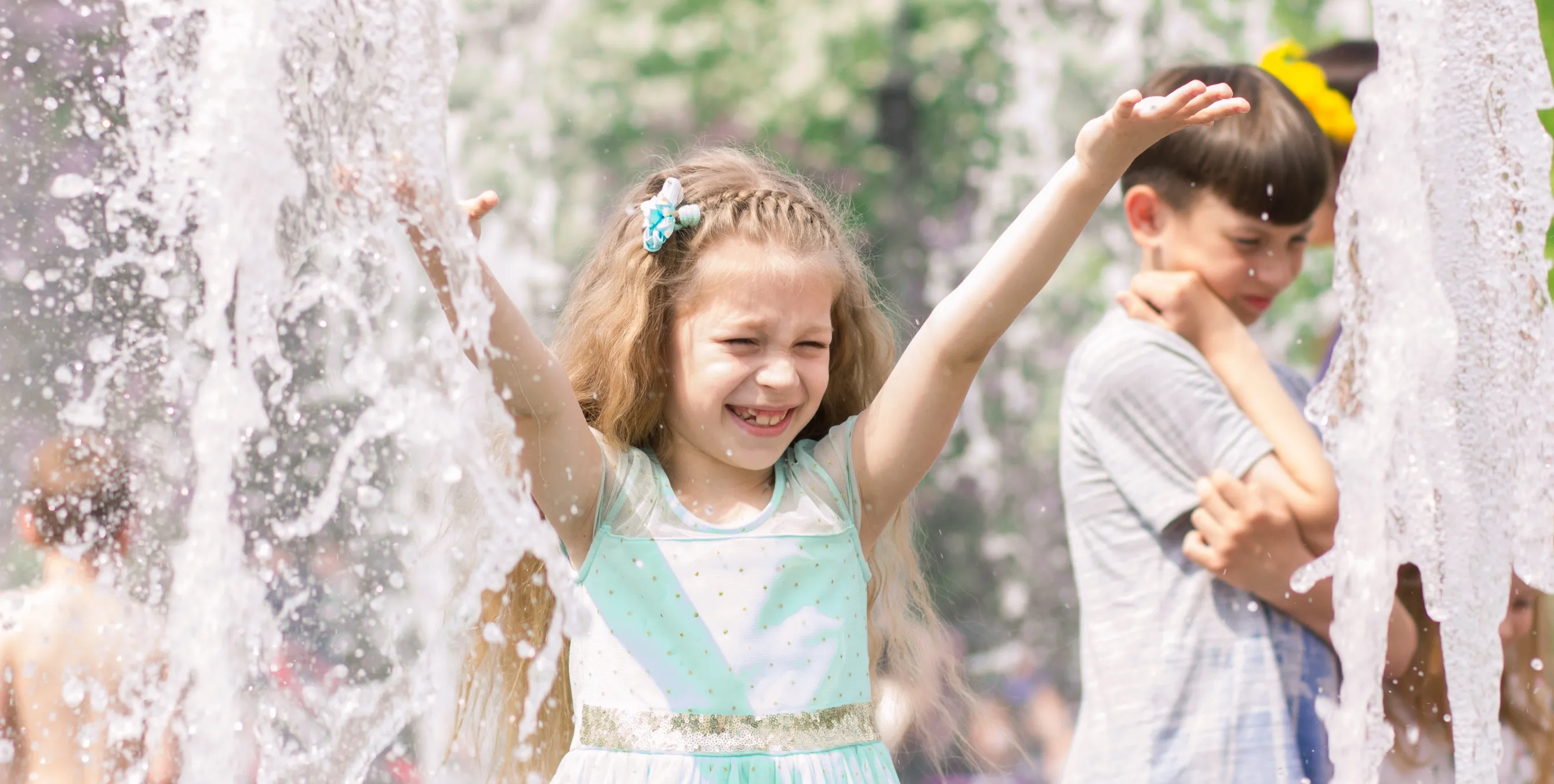 Mädchen spielt zwischen Wasserfontänen auf Wasserspielplatz
