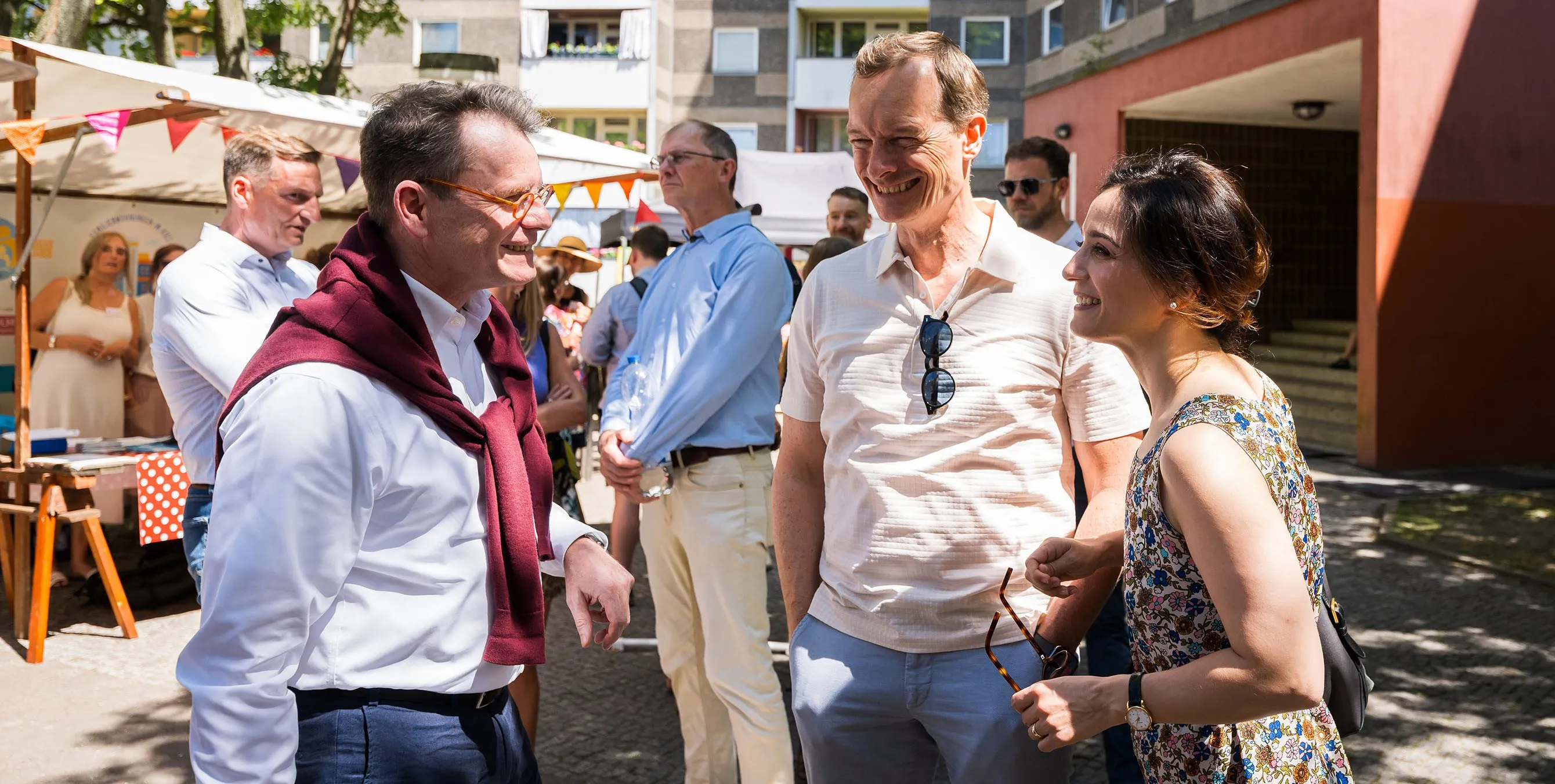 Zwei Männer und eine Frau bei einem Gespräch auf einem Quartiersfest im Freien. Alle drei lächeln. Foto: City-Press GmbH
