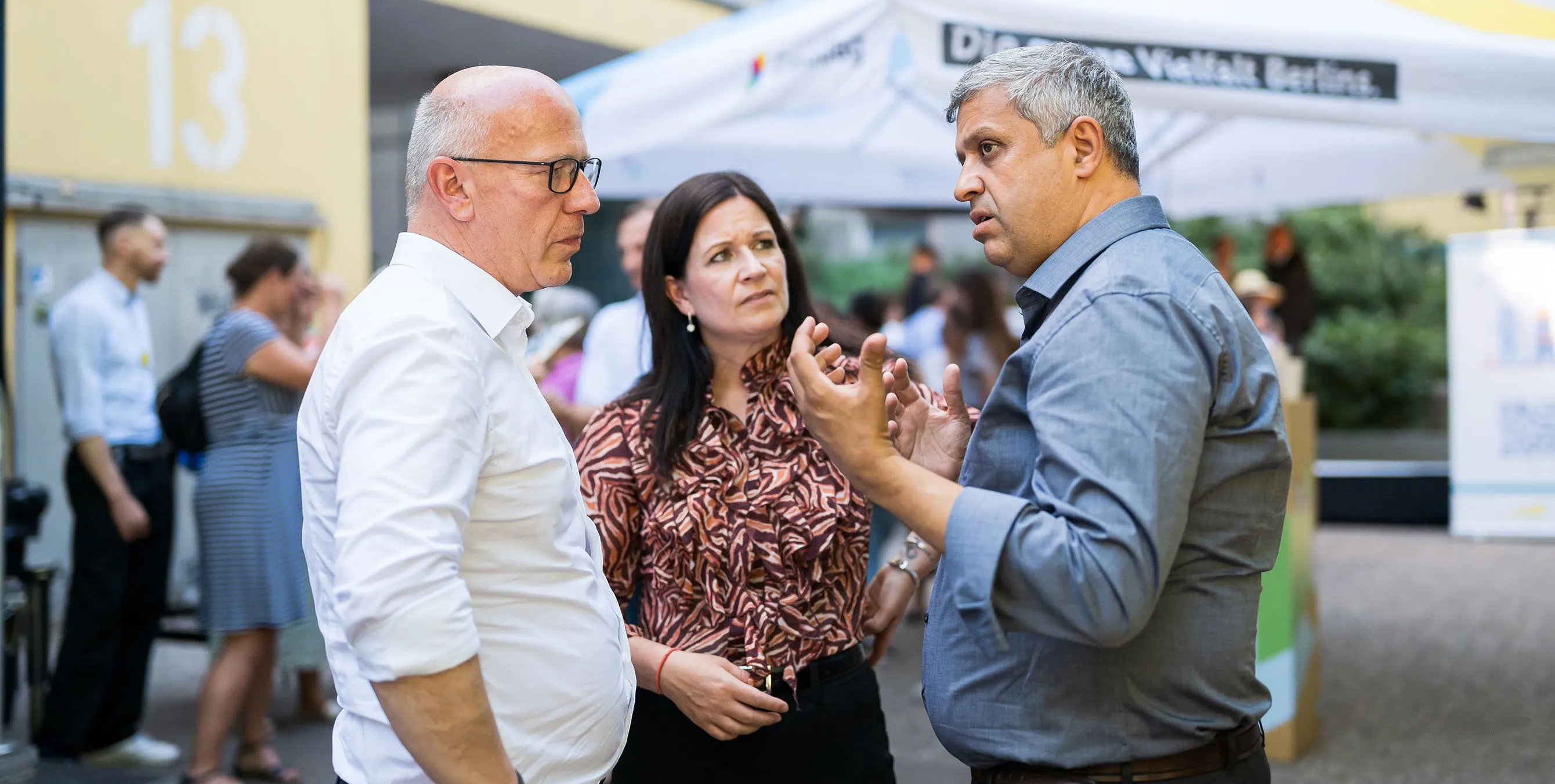 Zwei Männer und eine Frau stehen bei einem Fest im Freien zusammen und unterhalten sich. Foto: City-Press GmbH