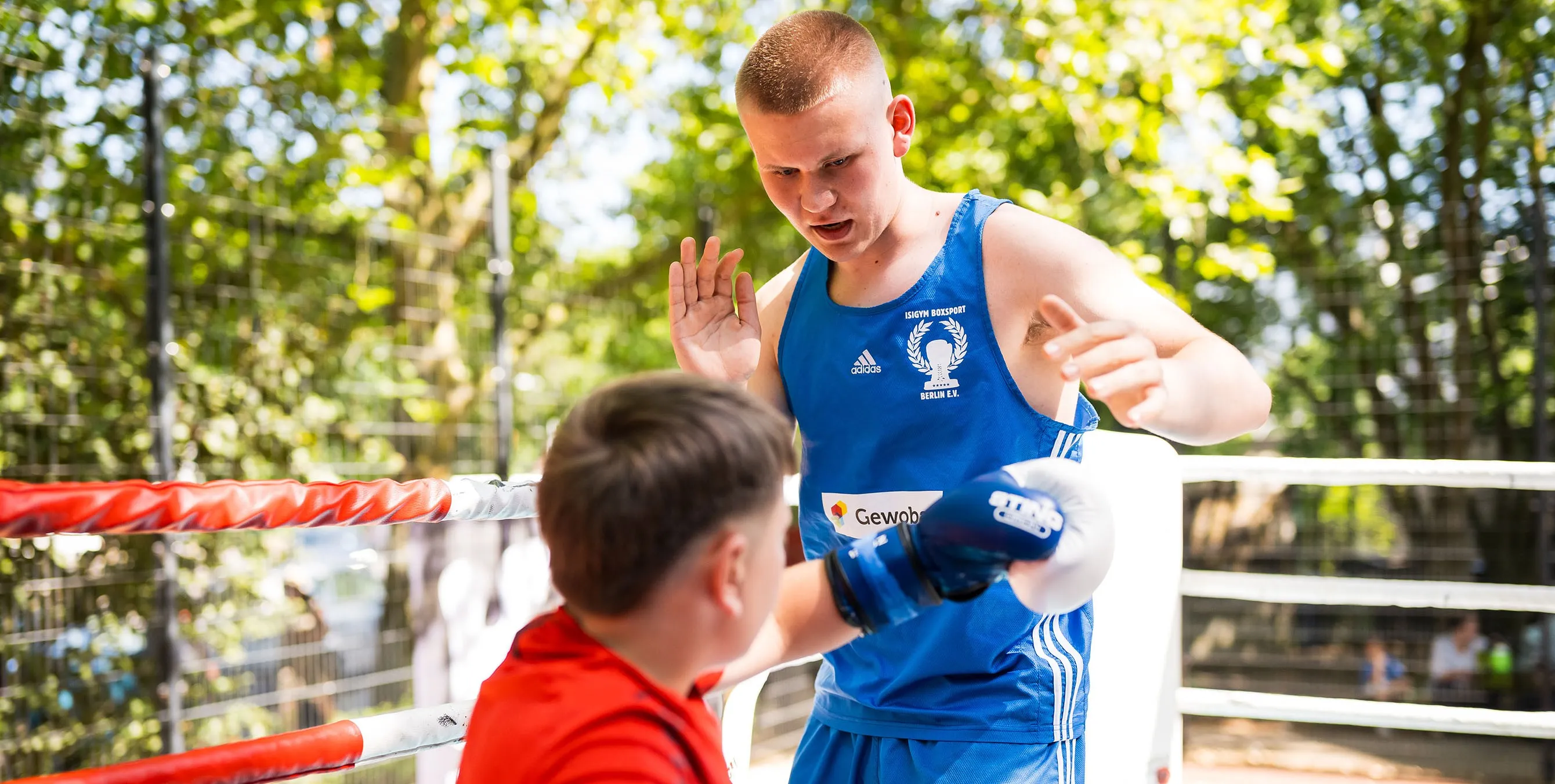 Szene eines Boxtrainings im Freien: Ein junger Boxer macht im Ring eine Übung mit einem Kind. Foto: City-Press GmbH