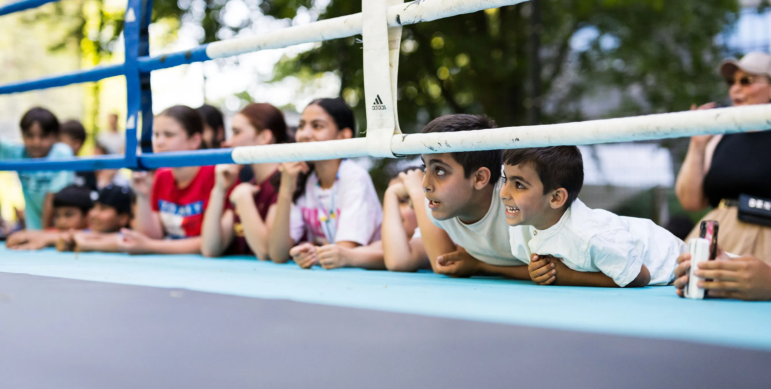 Szene von einem Quartiersfest: Rund zehn Kinder lehnen sich von außen an eine Boxring und schauen gespannt unter den Ringseilen hindurch. Foto: City-Press GmbH