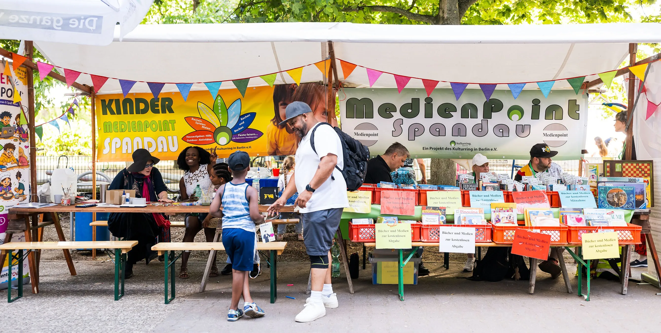 Szene von einem Quartiersfest im Freien: zwei nebeneinander aufgebaute Stände. Auf den dazugehörigen Bannern ist "Medienpoint Spandau" zu lesen. Foto: City-Press GmbH