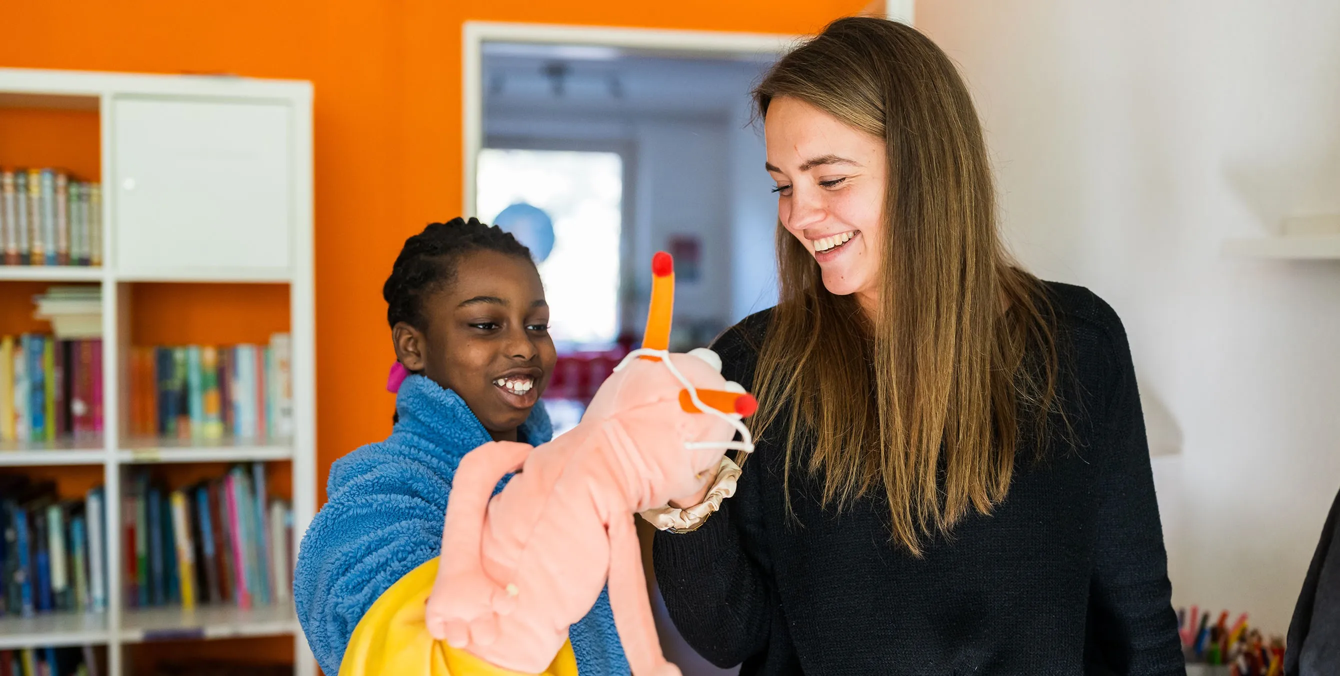 Eine Frau und ein Mädchen stehen in einer Wohnung und lachen. Das Mädchen trägt eine Handpuppe. Foto: City-Press GmbH