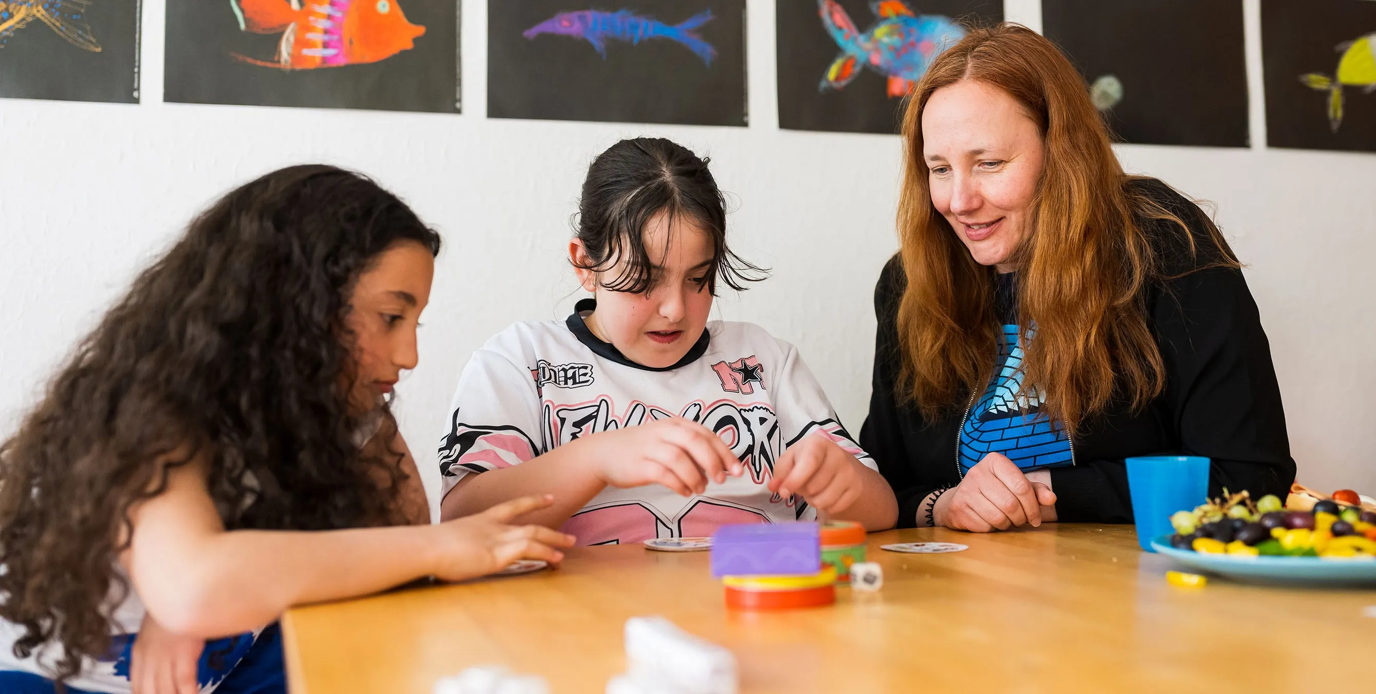Eine Frau sitzt mit zwei Mädchen an einem Esstisch. Gemeinsam spielen sie ein Gesellschaftsspiel. Foto: City-Press GmbH