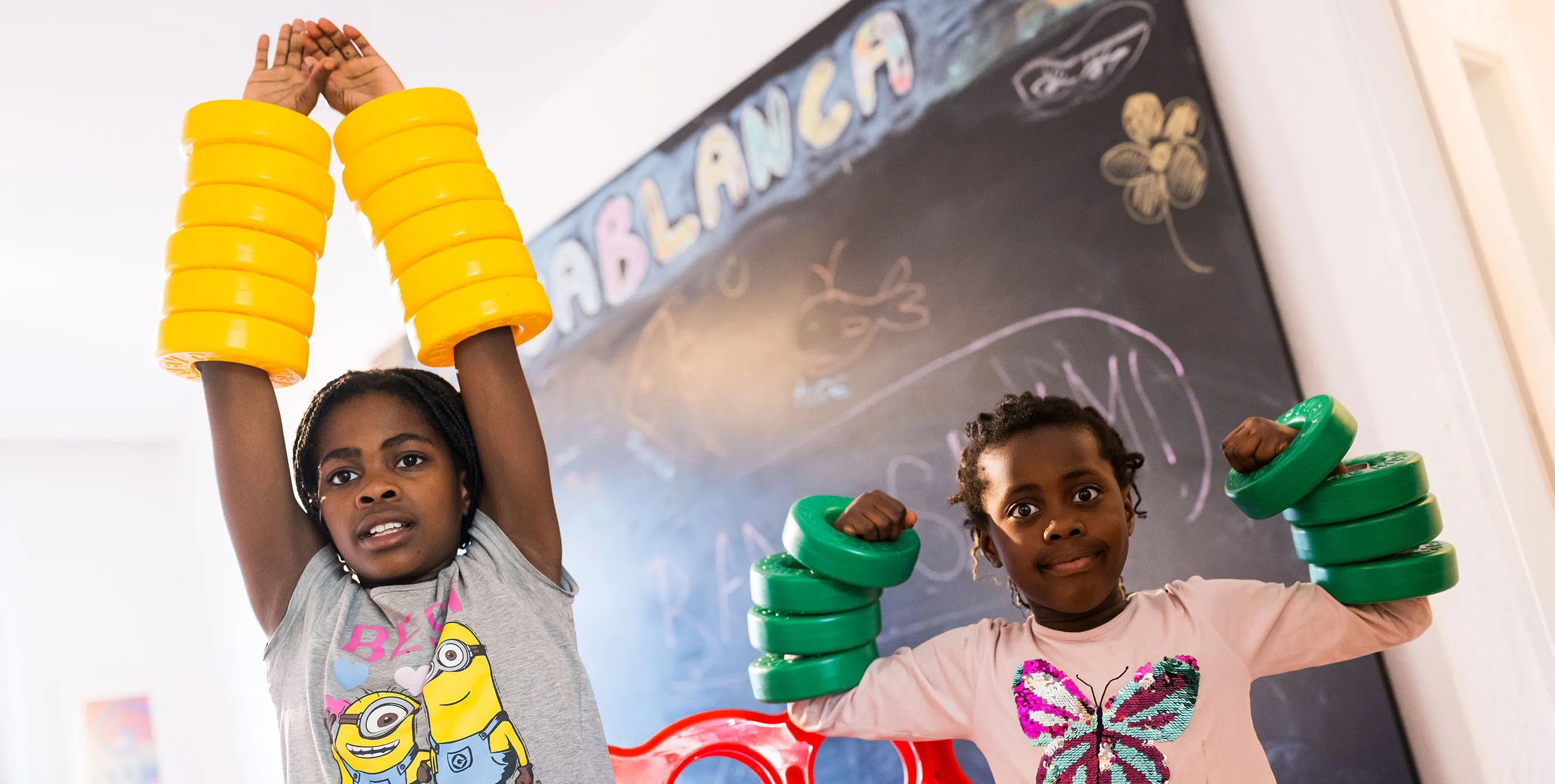 Zwei Mädchen in einem Spielraum. Über ihre Arme haben sie große, farbige Plastikringe gestülpt. Foto: City-Press GmbH