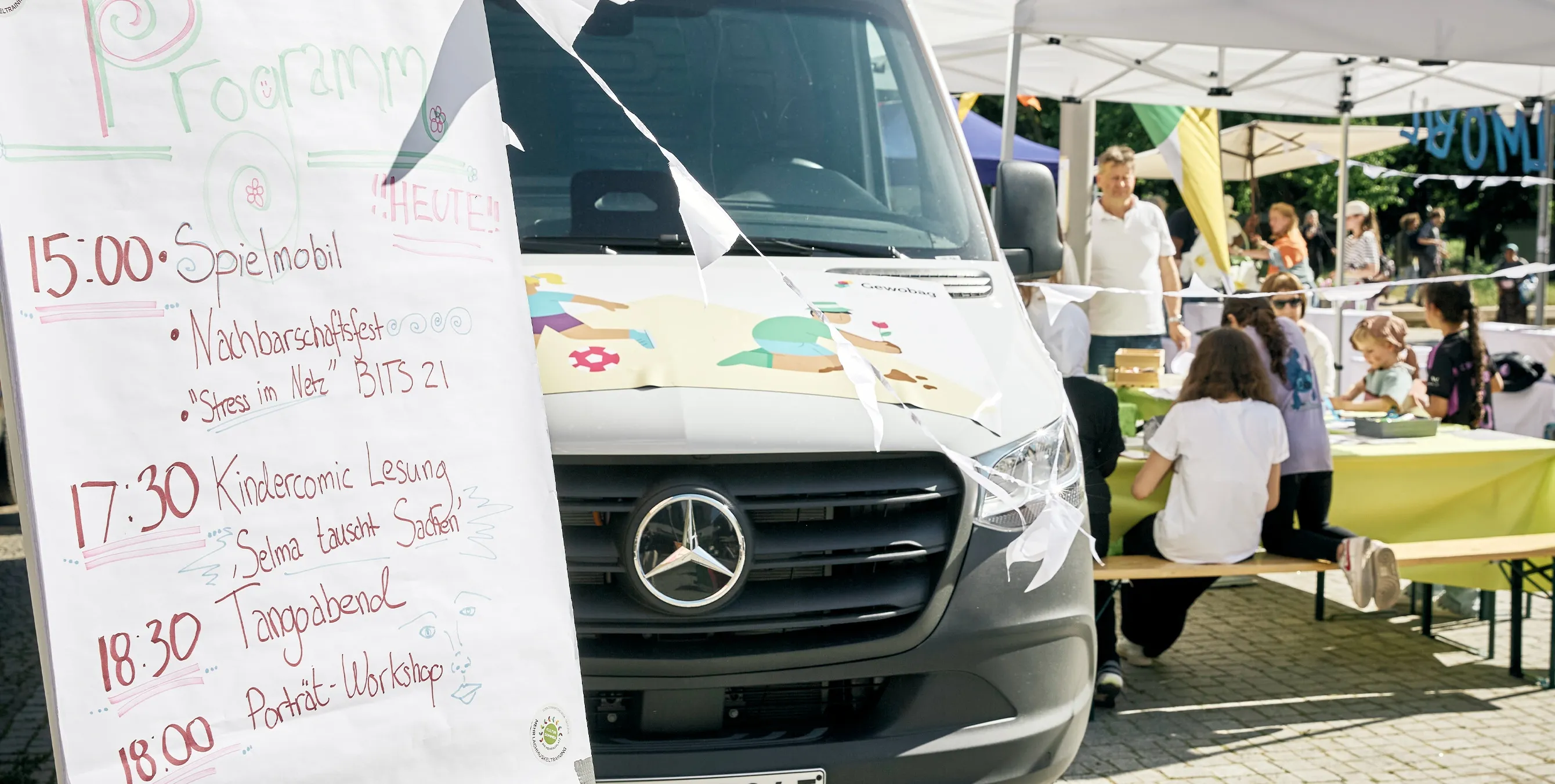 Großaufnahme eines handbeschriebenen Programmschilds auf einem Quartiersfest. Im Hintergrund sind Kinder an einem Basteltisch zu sehen. Foto: Britta Leuermann