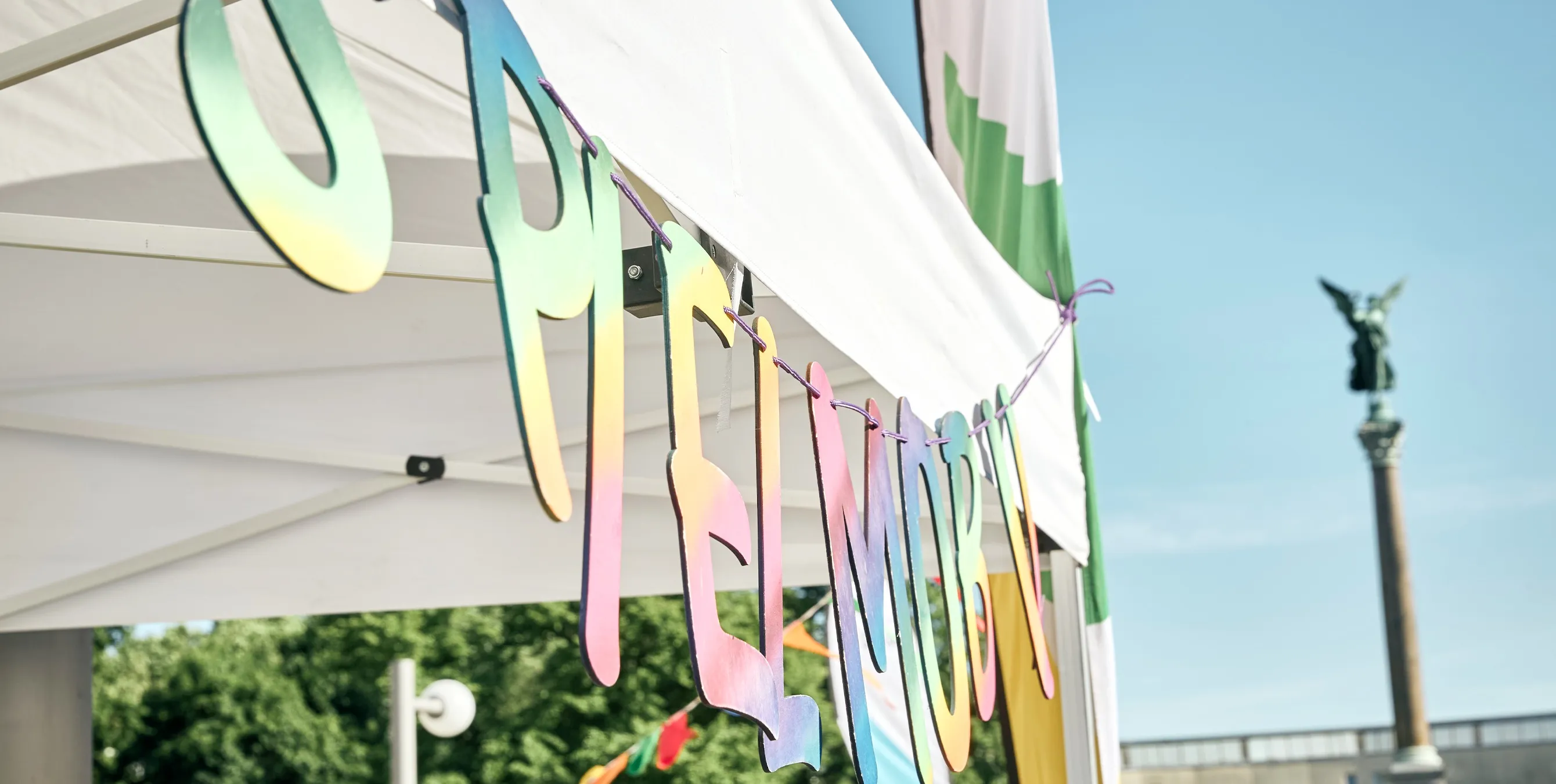 Großaufnahme: An einem Pavillon hängt in großen Buchstaben das Wort "Spielmobil". Im Hintergrund ist blauer Himmel und eine markante Säule zu sehen. Foto: Britta Leuermann