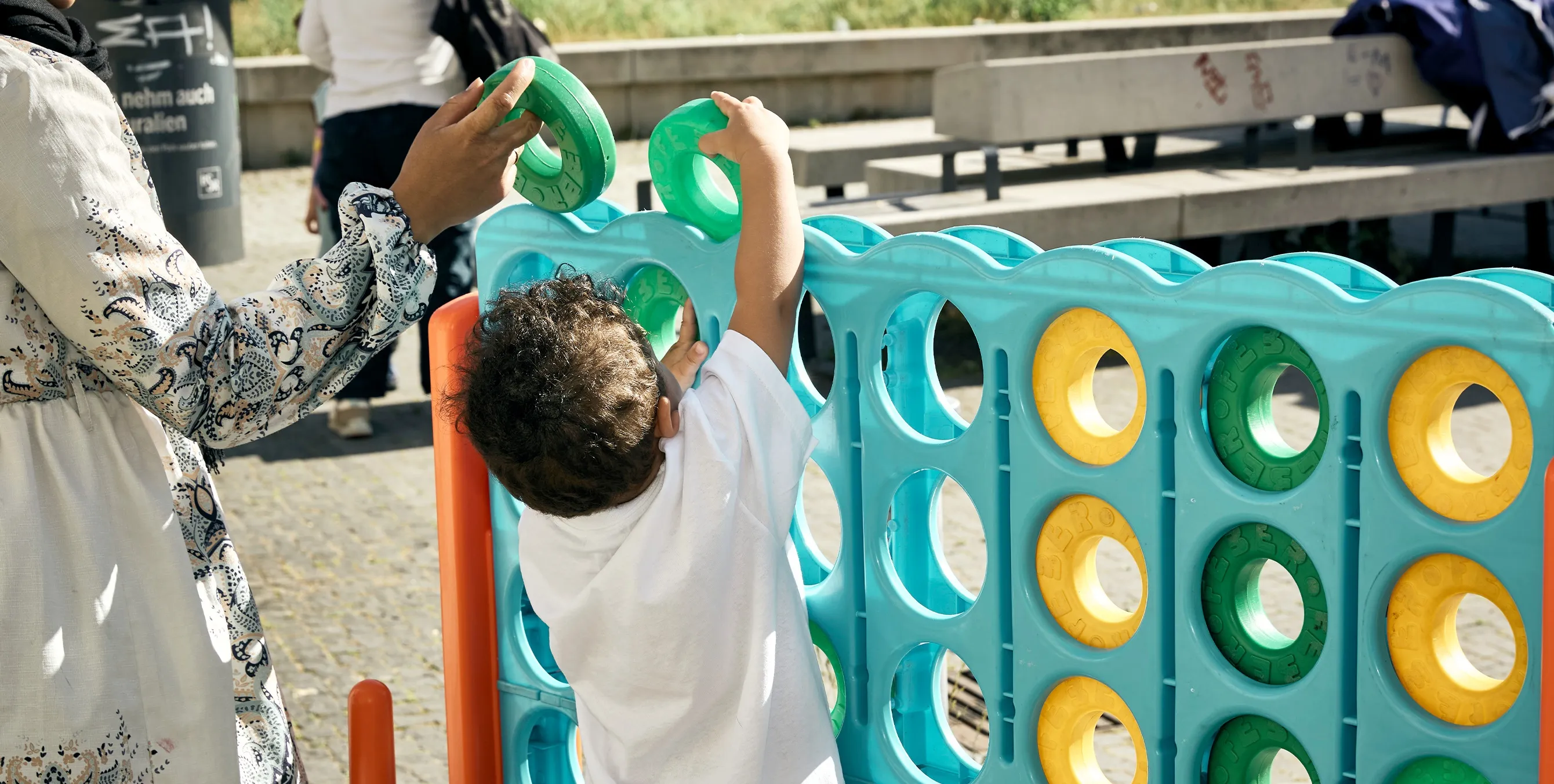 Aufnahme von hinten: Ein kleines Kind wirft einen Spielstein in ein überdimensionales "Vier gewinnt"-Spiel. Das Szene spielt sich auf einem öffentlichen Platz ab. Foto: Britta Leuermann