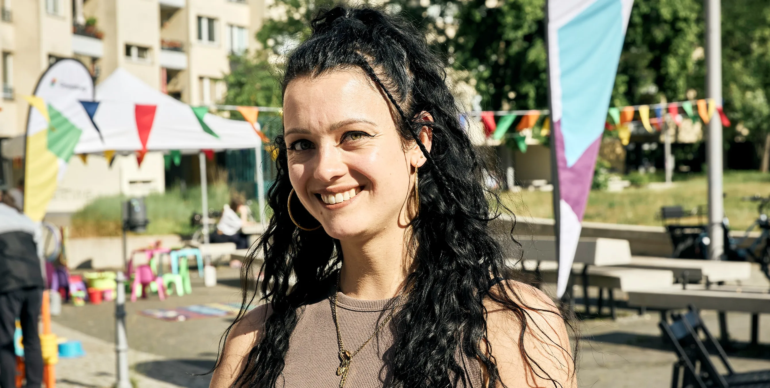 Eine junge Frau mit langen dunklen Haaren steht im Freien und lächelt in die Kamera. Im Hintergrund ist die Szenerie eines Kiezfestes zu erkennen. Foto: Britta Leuermann