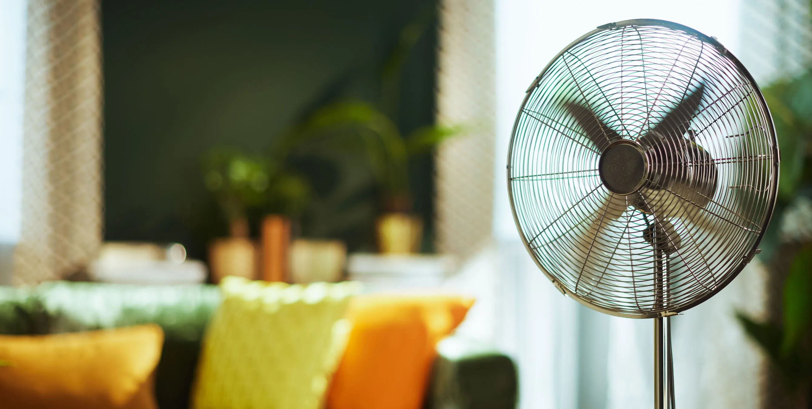Ein metallischer Ventilator vor einem Sofa in einer Wohnung. Foto: AdobeStock