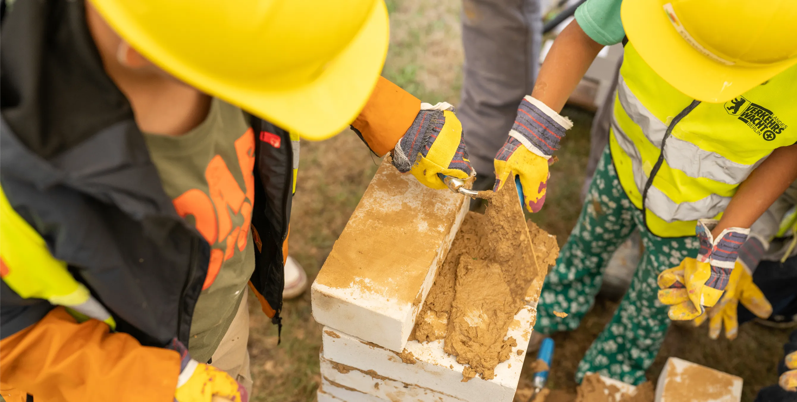 Großaufnahme vom Tag der kleinen Bauprofis: Zwei Kindern bauen mit Steinen, Lehm und Maurerkelle eine kleine Wand. Foto: Ralph Maak 