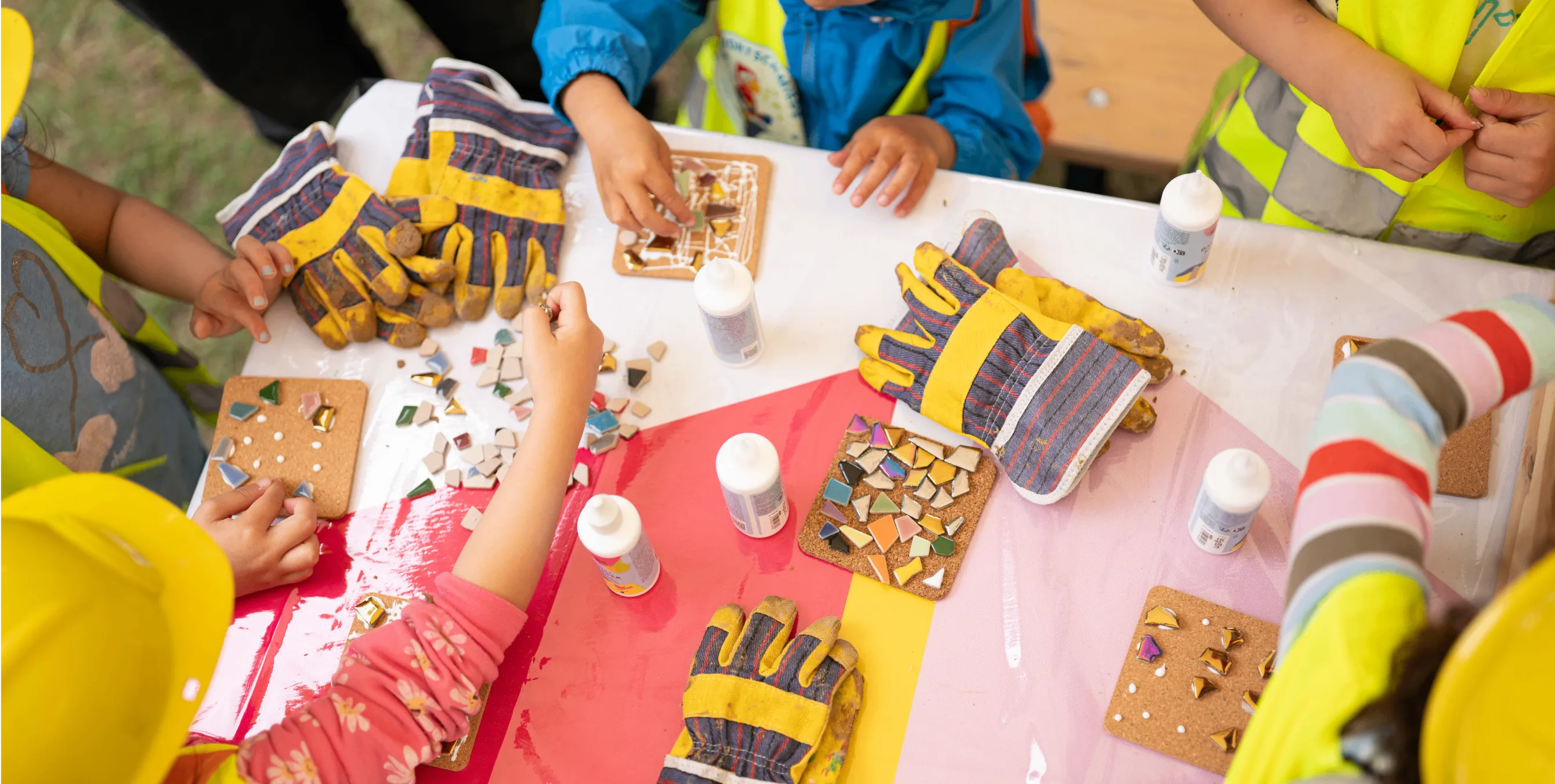 Großaufnahme vom Tag der kleinen Bauprofis: mehrere Kinderhände an einem Aktionstisch, an dem mit Mosaiksteinchen gewerkelt wird. Foto: Ralph Maak 