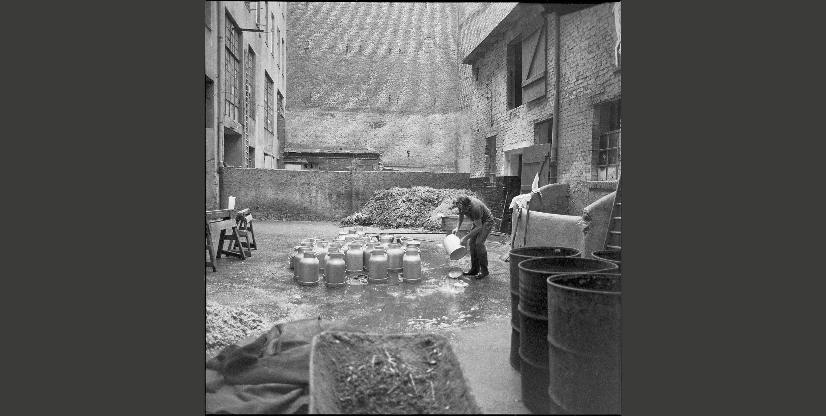 Historisches Schwarz-Weiß-Foto: ein Mann in einem Innenhof, in dem diverse Milchkannen stehen. Foto: Landesarchiv Berlin