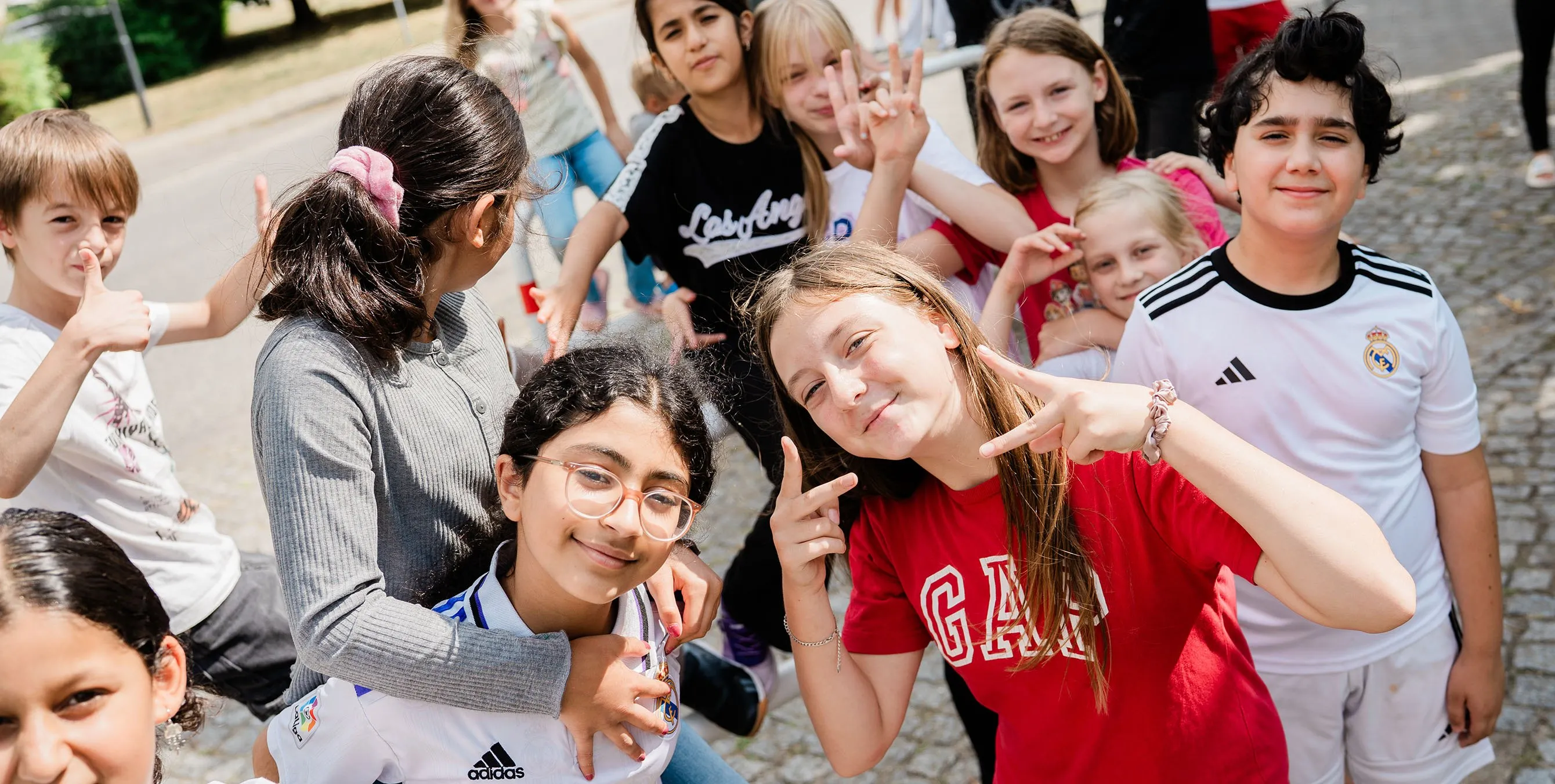 Eine Horde Kinder macht verschiedene Gesten mit den Händen und lächelt in die Kamera. Foto: Johannes Karnauchow/3viertel3