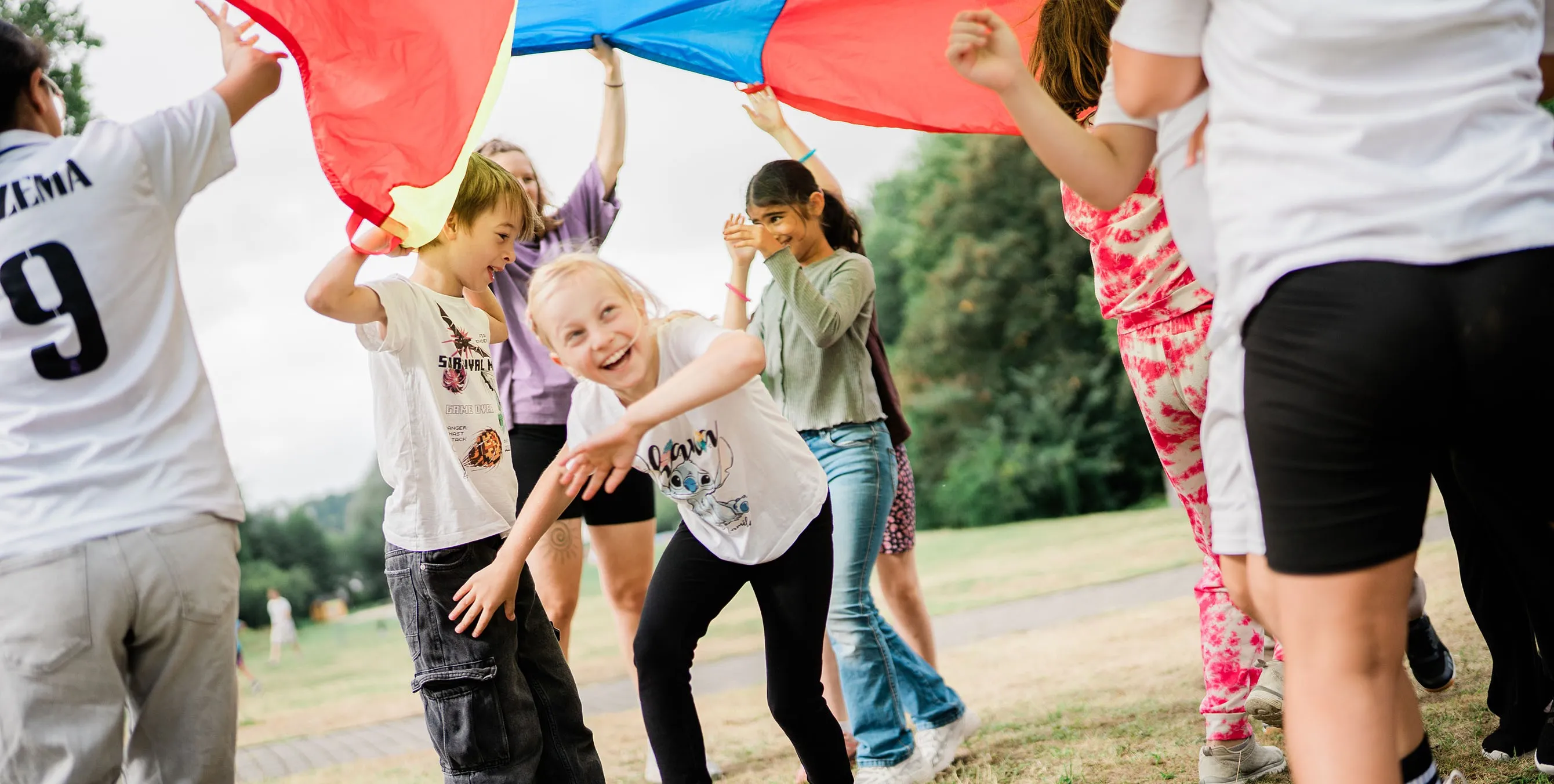 Lachende Kinder spielen im Freien mit einem bunten Schwungtuch. Foto: Johannes Karnauchow/3viertel3