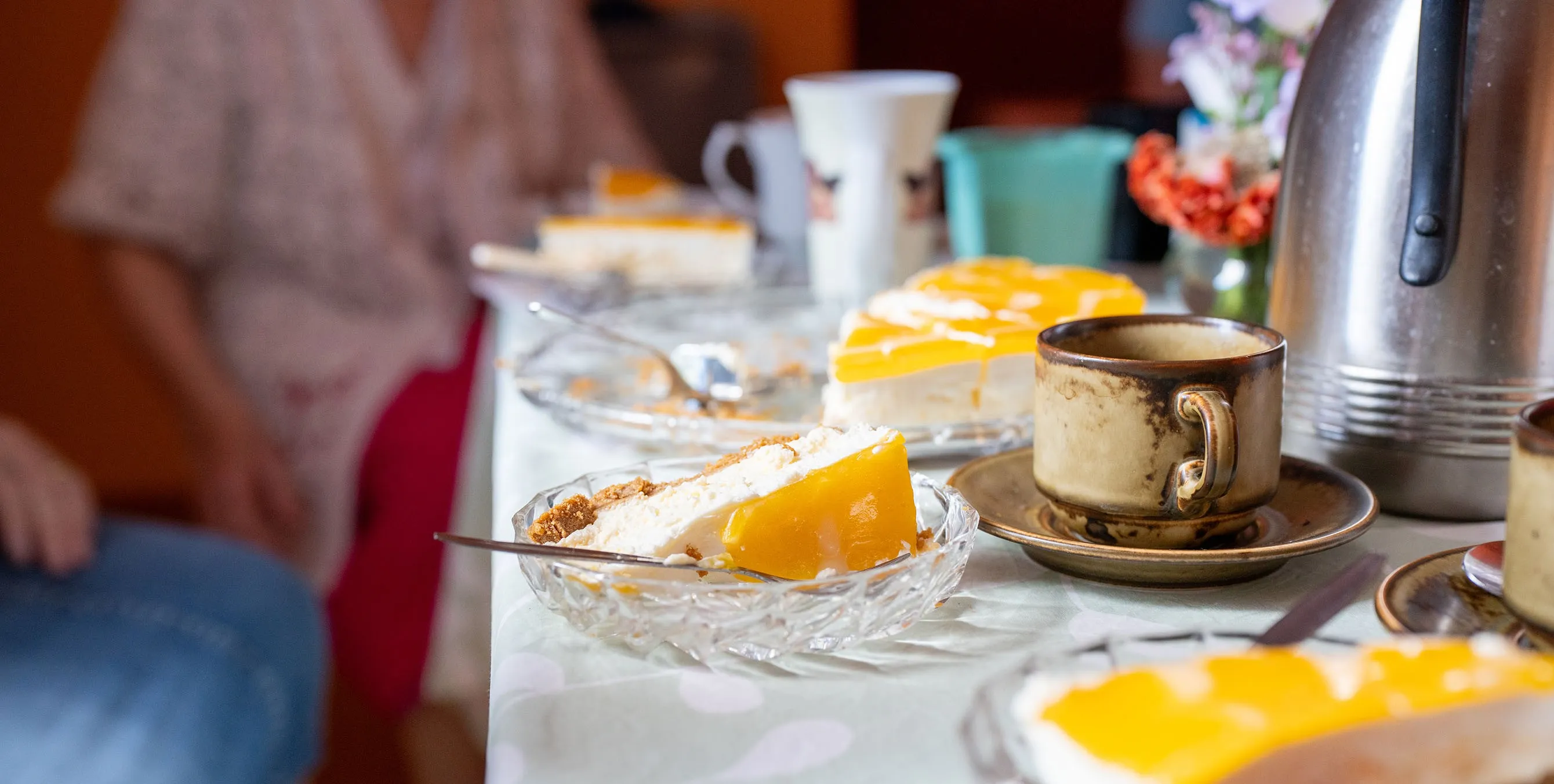 Detailaufnahme: ein Stück Kuchen in einem Glasteller und eine Kaffeetasse samt Untertasse, die auf einer gedeckten Kaffeetafel stehen. Foto: Ralph Maak