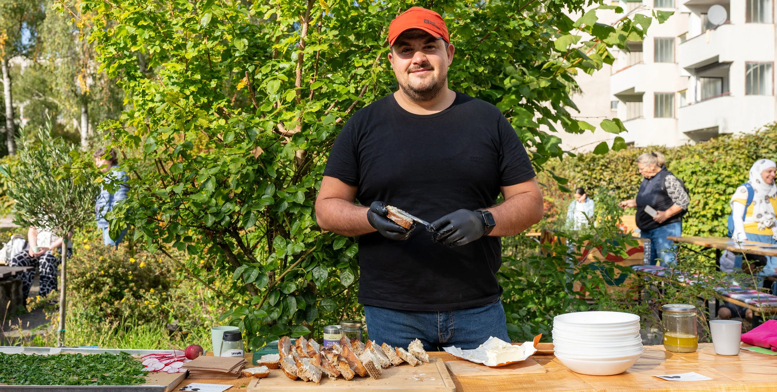 Mann mit roter Kappe bereitet belegtes Brot bei einem Gartenfest zu. Foto: Ralph Maak