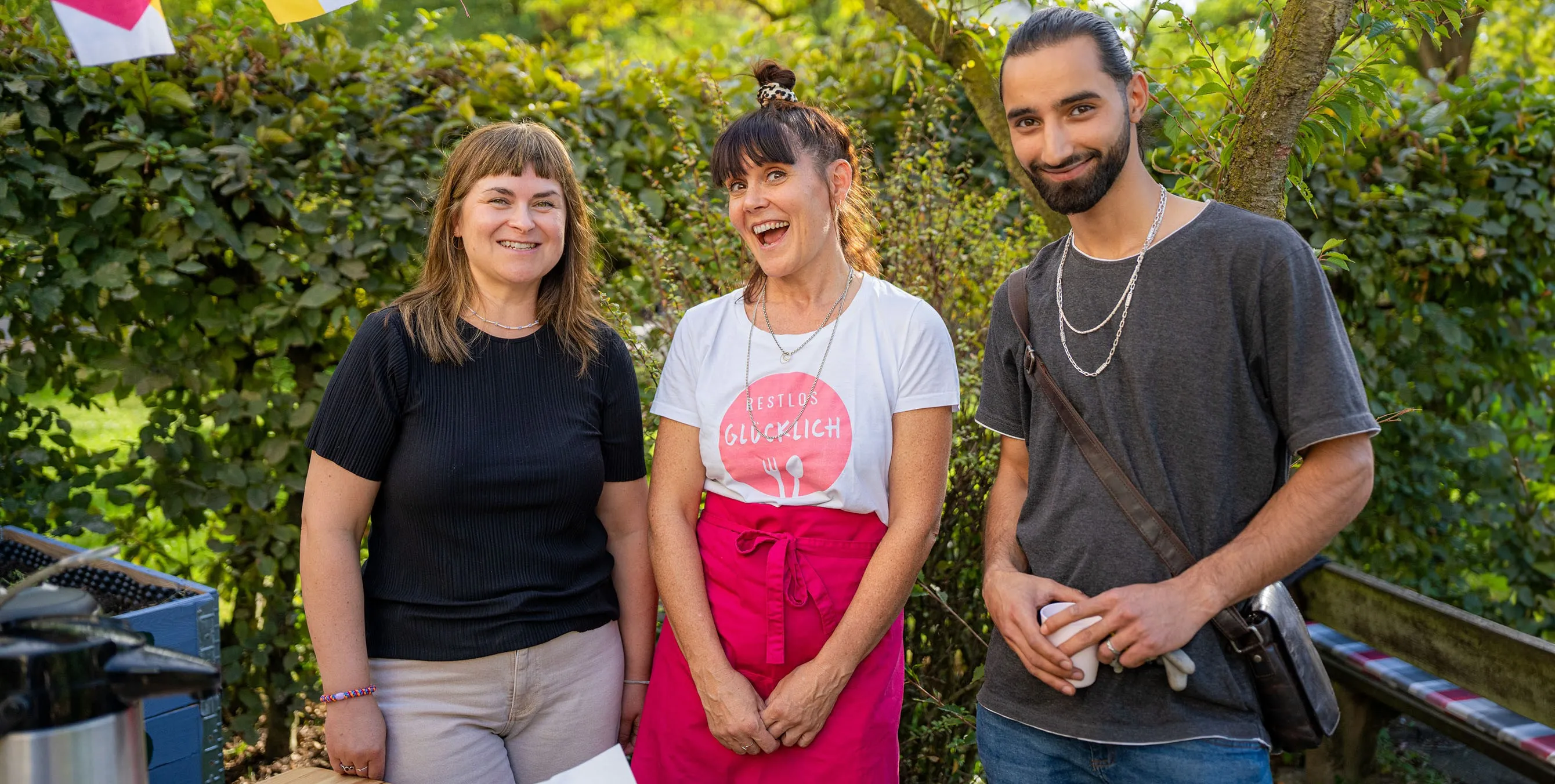 Drei Menschen stehen eng beisammen und lachen bei einem Gartenfest. Foto: Ralph Maak