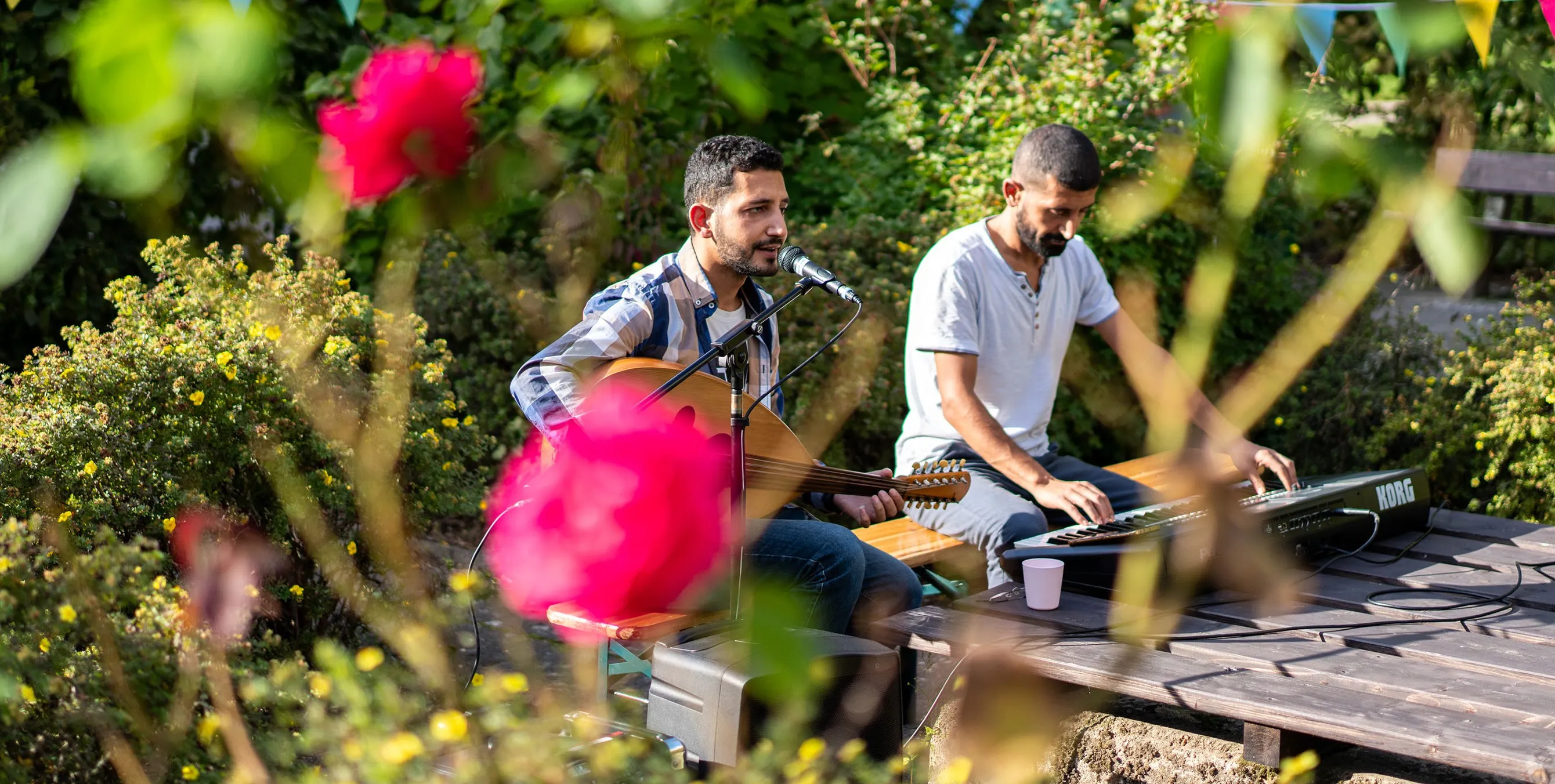 Zwei Musiker spielen im Garten, einer mit Saiteninstrument, einer am Keyboard. Foto: Ralph Maak
