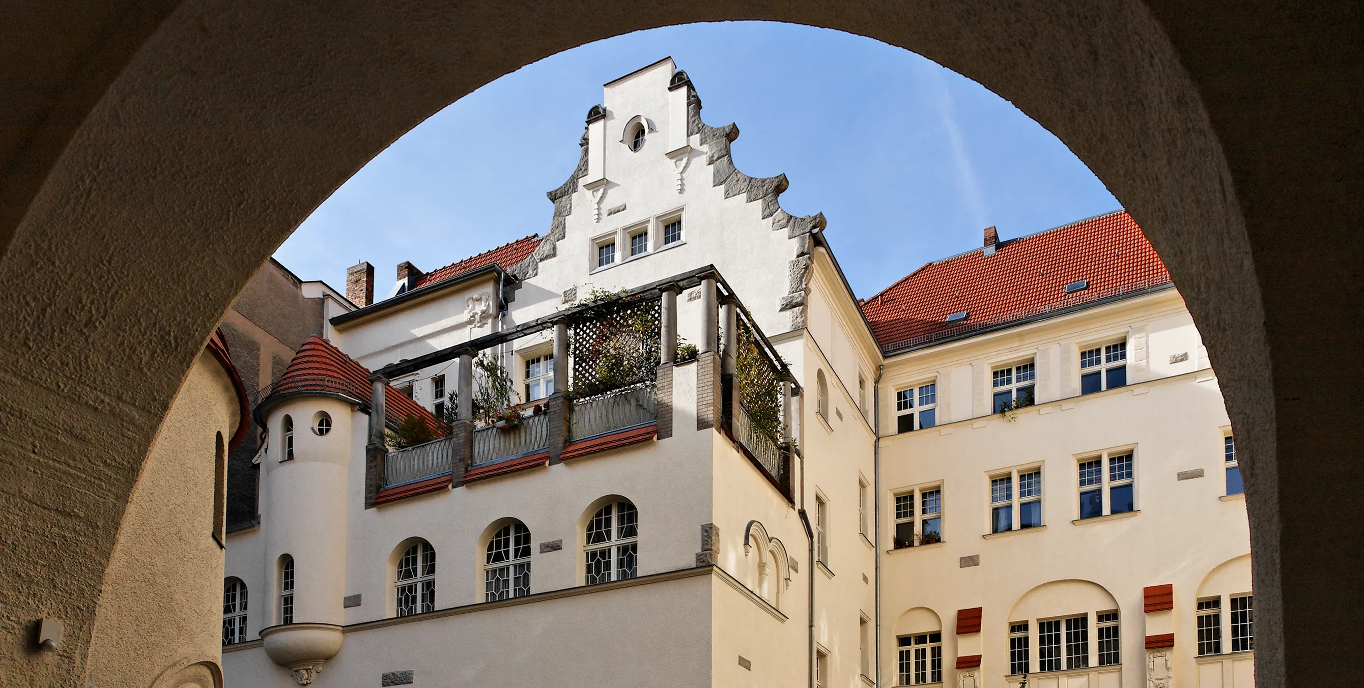Blick durch einen großen Torbogen in einen Innenhof. Darin: ein kunstvoll gestalteter Gebäudeteil samt Logia. Foto: Gewobag