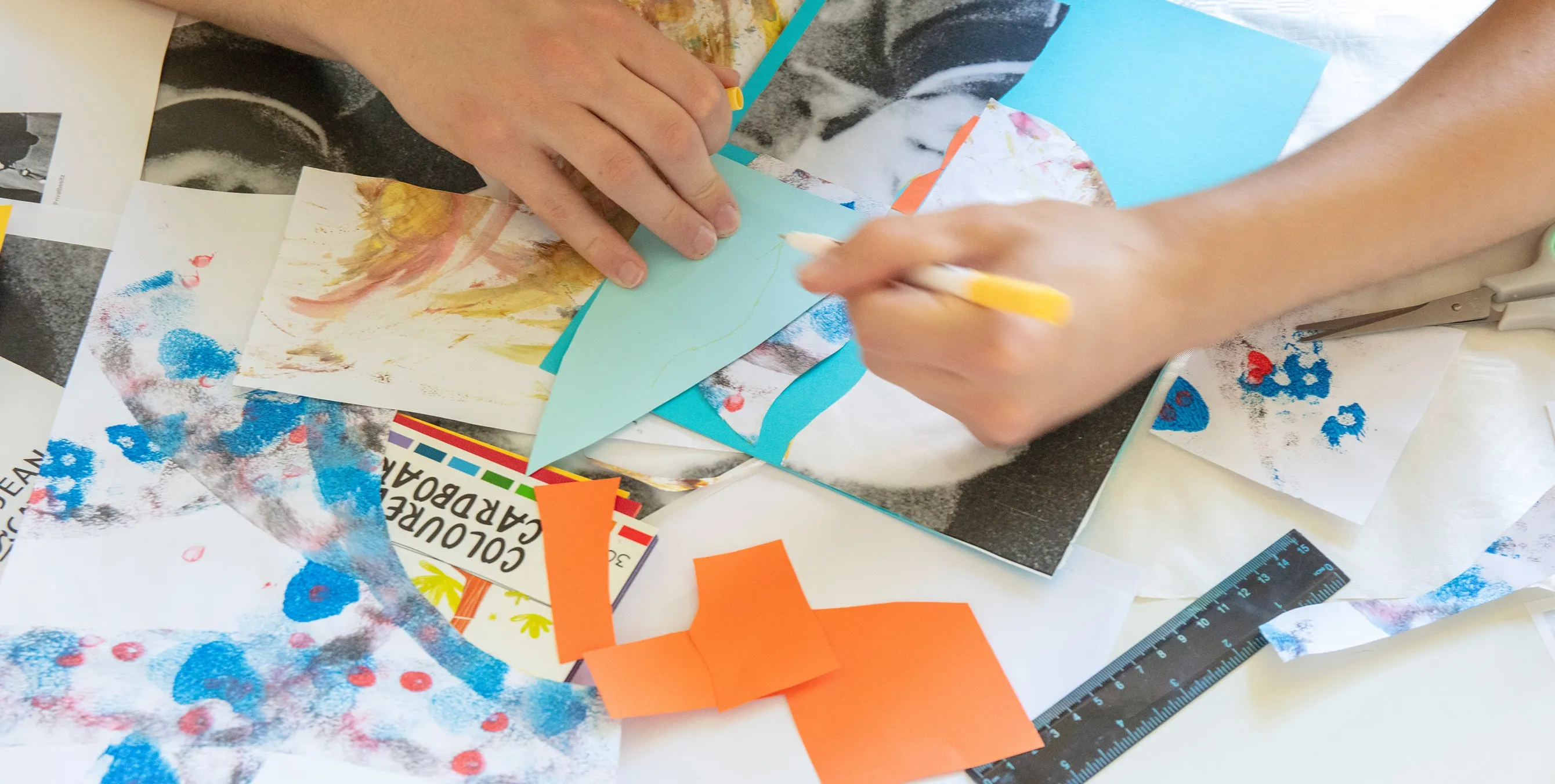Nahaufnahme: Eine Person sitzt an einem Tisch und bastelt an einer Collage. Foto: Ludger Paffrath