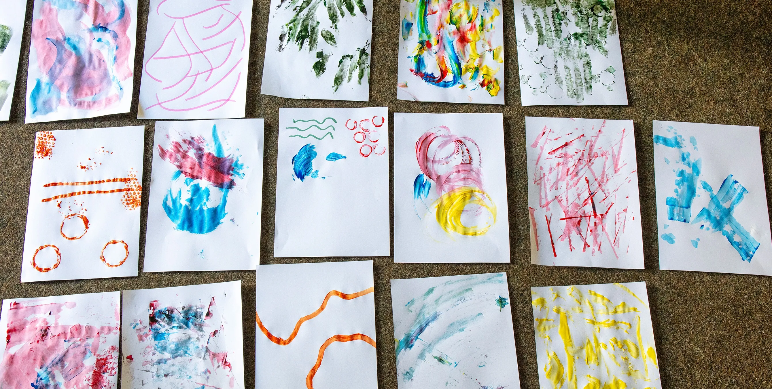 Gut 20 weiße Papierblätter, die auf unterschiedliche Art und Weise mit Tusche bemalt wurden, liegen nebeneinander auf einem Teppich. Foto: Ludger Paffrath